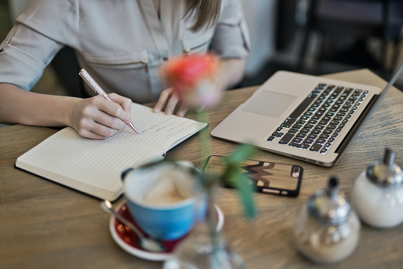 person writing on a notebook besides a laptop